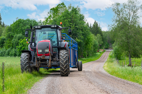 Tractor And Trailer standing near the road in farm during harvesting work in summer under sky with clouds near forest