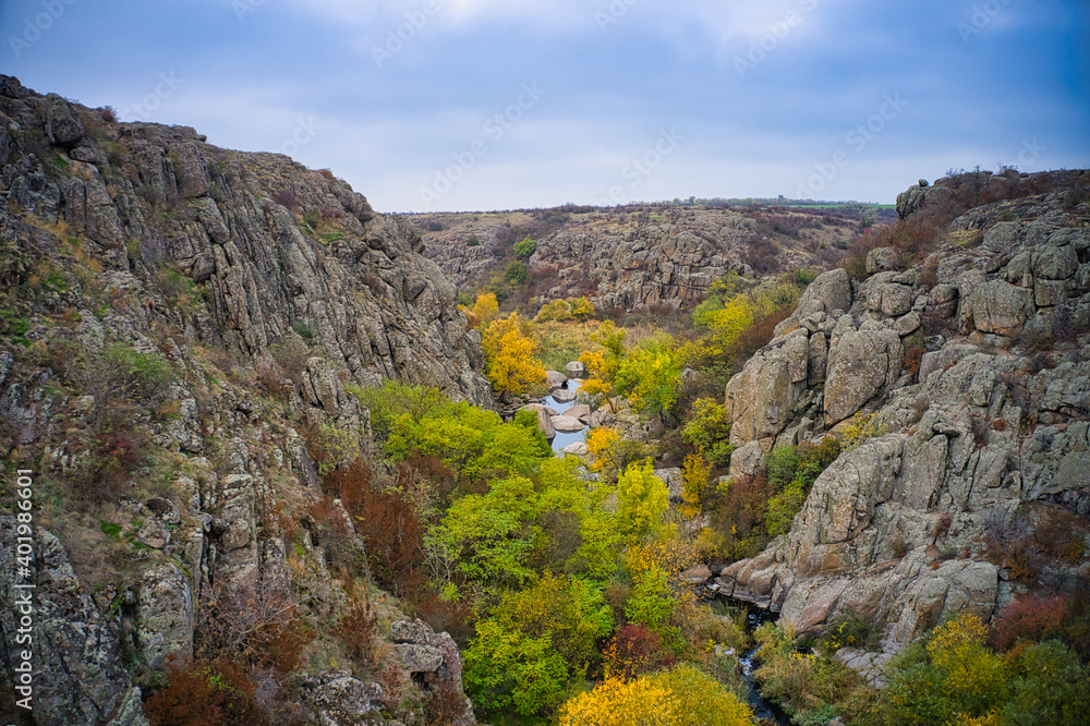 A picturesque stream flows in the Aktovsky Canyon, surrounded by autumn trees and large stone boulders