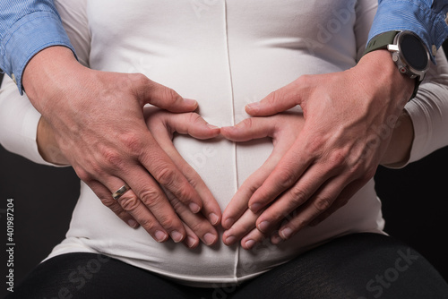 Die werdenden Eltern halten gemeinsam ihre Hände in Herzform über den Schwangerschaftsbauch der baldigen Mutter
