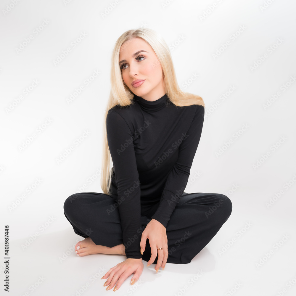 Blondes Fotomodel mit heller Hautfarbe in schwarzer Kleidung sitzt vor einem weissen Studiohintergrund Blondes Fotomodel mit heller Hautfarbe in schwarzer Kleidung sitzt vor einem weissen Studiohintergrund