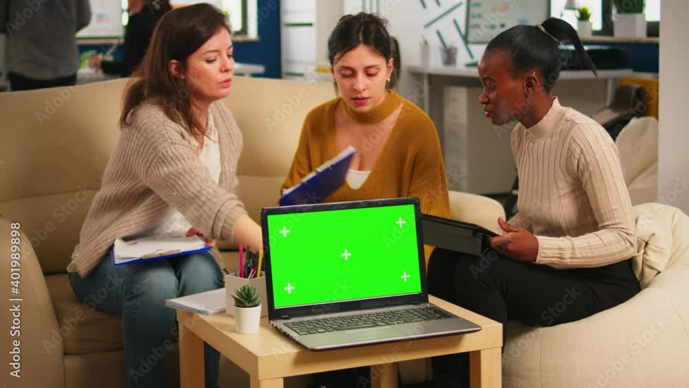 Diverse women sitting at table in start up office discussing strategy with green screen laptop in front of camera. Lady explaining to multiethnic team new project, chroma key display. mock up monitor Diverse women sitting at table in start up office discussing strategy with green screen laptop in front of camera. Lady explaining to multiethnic team new project, chroma key display. mock up monitor
