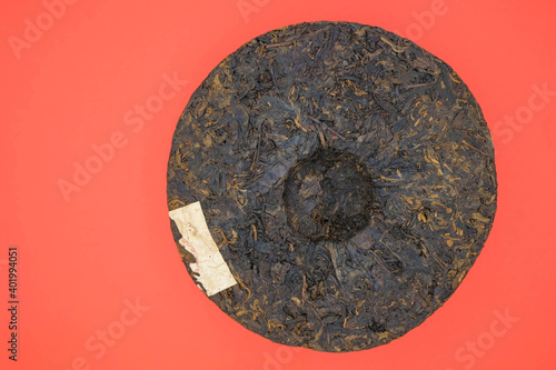 Round flat disc of puer tea isolated on a red background. Pressed Chinese fermented Pu-erh tea. Minimalism. Copy space. 