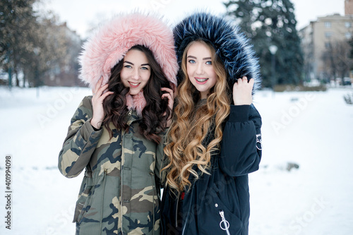 Young two woman winter portrait. Shallow dof. Beautiful smiling face of fashion model with red lips and fur hood