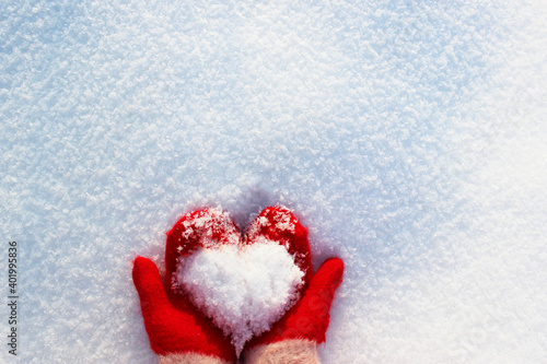 hands in knitted mittens with a heart made of snow on a winter day. ... Snowy heart in hands. Human hands in warm red mittens with a snowy heart on a background of snow. Love winter christmas or