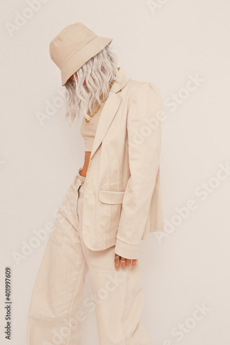 Urban street style Blonde Girl in white studio. Details of everyday look. Casual beige outfit and accessories. Bucket hat. Trendy Minimalist fashion photo