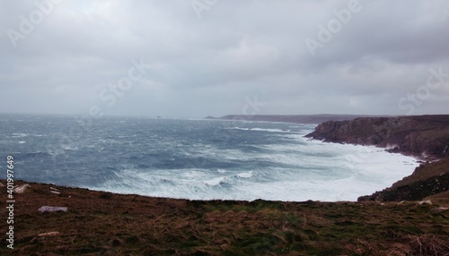 Stormy rough seas and breaking Atlantic ocean waves over rocks at Lands End Cornwall, UK after Storm Bella gale force winds surge through the coastline.