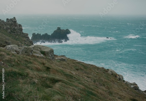 Stormy rough seas and breaking Atlantic ocean waves over rocks at Lands End Cornwall, UK after Storm Bella gale force winds surge through the coastline.