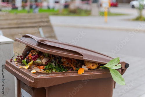 Brimful municipal bio-waste trash can with open lid for biological organic waste standing on open street in residential area after christmas holidays