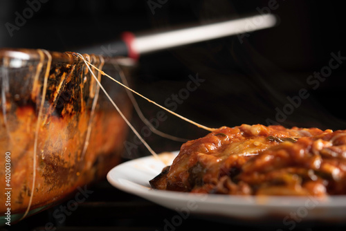 Baked Eggplant Parmagiana From Oven With Red Sauce and Cheese Being Served on White Plate photo