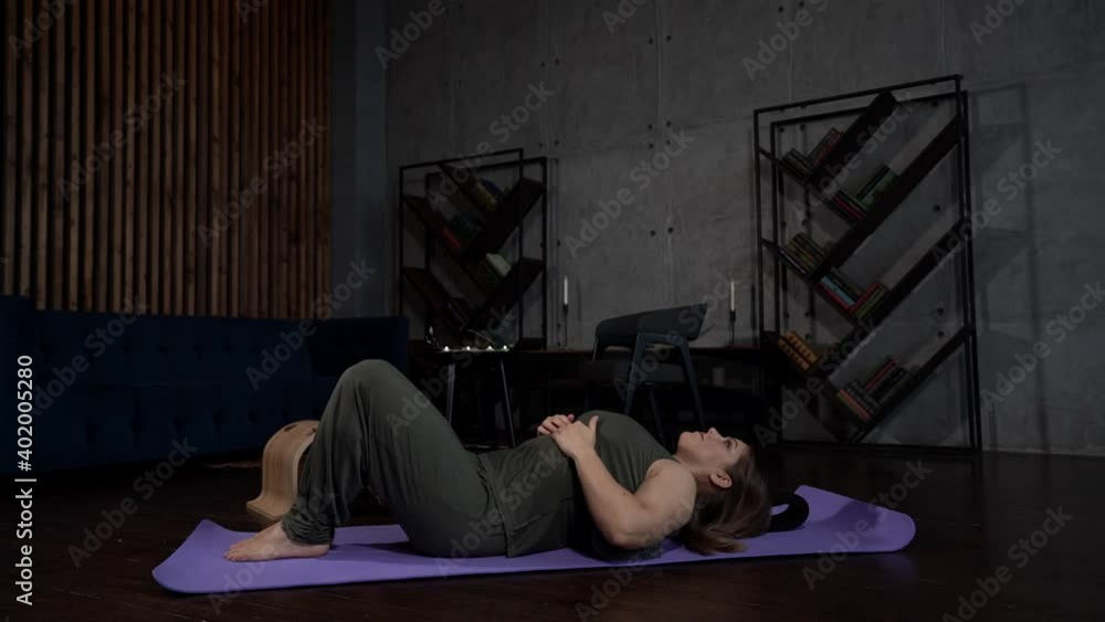 A woman prepares to do exercises on a Mat at home, side View. She put a roller under her head. Sports and fitness. The concept of training, training and Wellness. A woman prepares to do exercises on a Mat at home, side View. She put a roller under her head. Sports and fitness. The concept of training, training and Wellness.