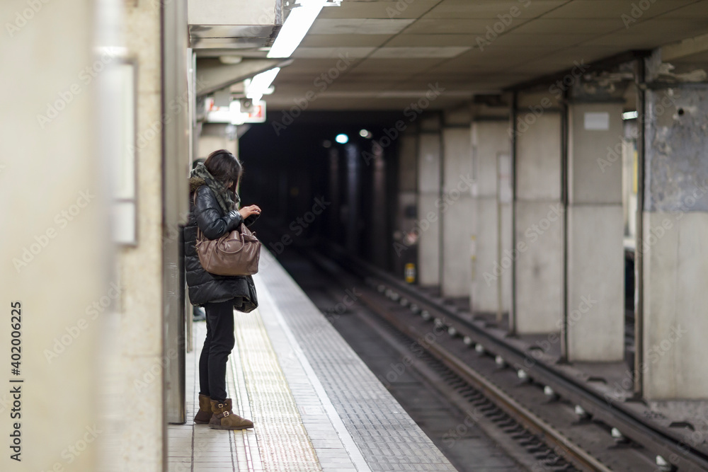 woman using her smartphone on platform, traveling on train, metro, subway, underground station in winter season with shallow depth of field
