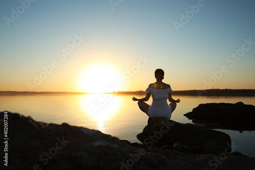 Woman practicing yoga near river on sunset. Healing concept