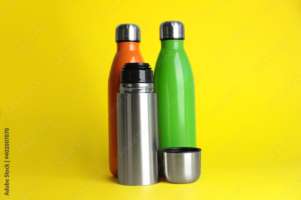 Stylish stainless thermo bottles on yellow background Stylish stainless thermo bottles on yellow background