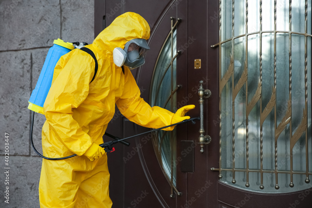 Person in hazmat suit disinfecting entrance door with sprayer. Surface treatment during coronavirus pandemic Person in hazmat suit disinfecting entrance door with sprayer. Surface treatment during coronavirus pandemic