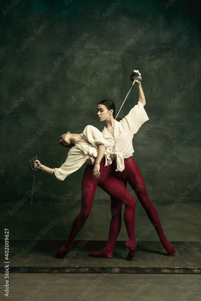 Death. Two young female ballet dancers like duelists with swords on dark green background. Caucasian models dancing together. Ballet and contemporary choreography concept. Creative art photo. Death. Two young female ballet dancers like duelists with swords on dark green background. Caucasian models dancing together. Ballet and contemporary choreography concept. Creative art photo.