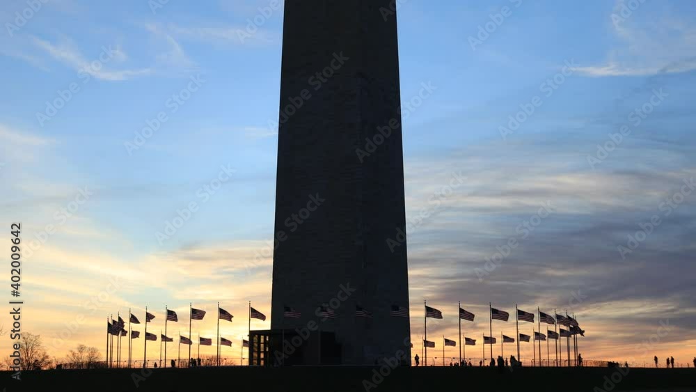 Silhouette of Washington Monument base, American flags and tourists at sunset in Washington, D.C.