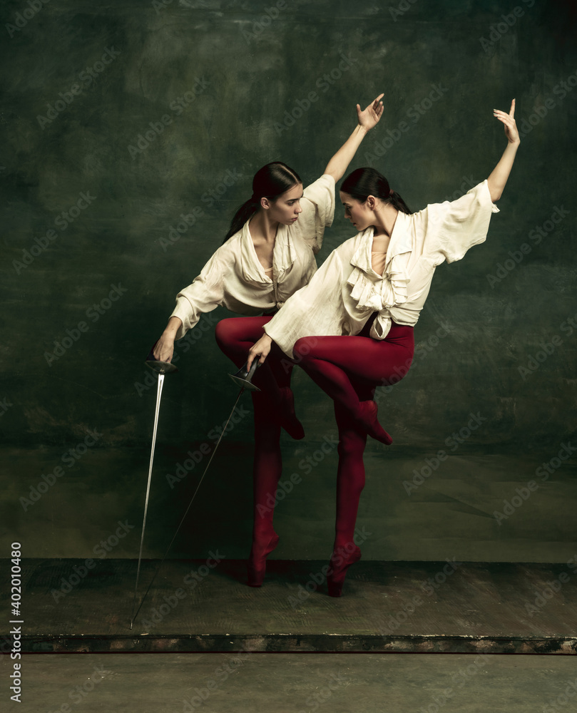 Birds. Two young female ballet dancers like duelists with swords on dark green background. Caucasian models dancing together. Ballet and contemporary choreography concept. Creative art photo.