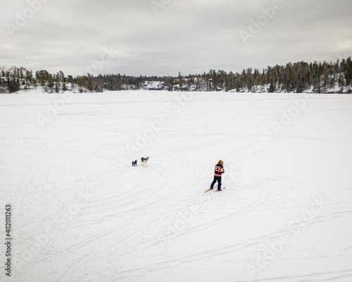 Man walking across frozen lake in northern Canada in snowshoes with his husky wolf dog.