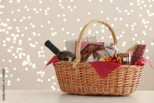Фотография Wicker basket with gifts, wine and food against blurred festive lights