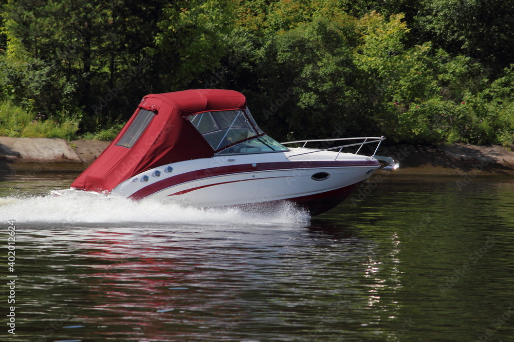 Fast gliding inboard motor boat with closed red tent side view on water at Sunny summer day, active private recreation boating on river