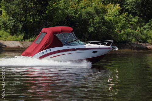 Fast gliding inboard motor boat with closed red tent side view on water at Sunny summer day, active private recreation boating on river
