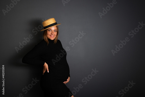 Pregnant woman with big belly wearing black dress posing at studio over dark background. Pregnancy. photo