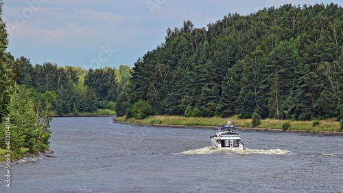 One white cabin motor boat floating on Moscow Canal water with green trees on shores at summer day, holiday river tourism private recreation
