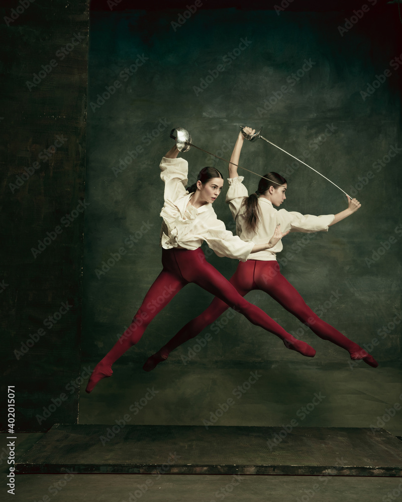 Fight. Two young female ballet dancers like duelists with swords on dark green background. Caucasian models dancing together. Ballet and contemporary choreography concept. Creative art photo.