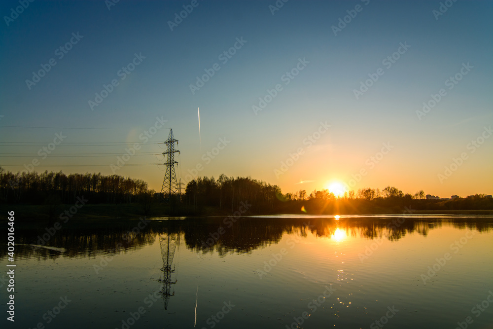 Sunset over lake and power line tower