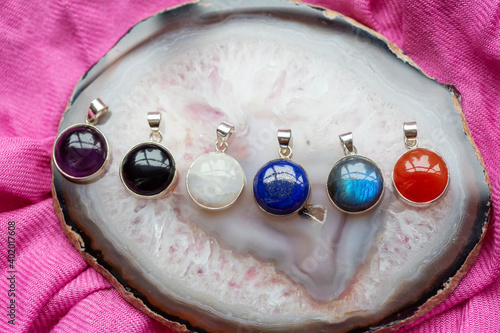 Collection of sterling silver pendants with various mineral stones on agate and pink textyle background photo