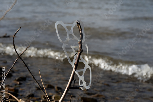 Littered Six Pack plastic can holder rings stuck on a branch off the shore фототапет