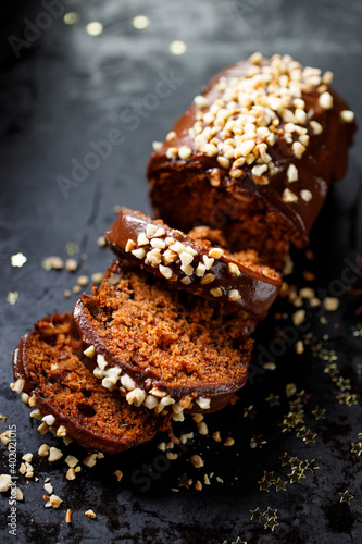 Traditional gingerbread cake with chocolate glaze sprinkled with chopped almonds on a black background close up view