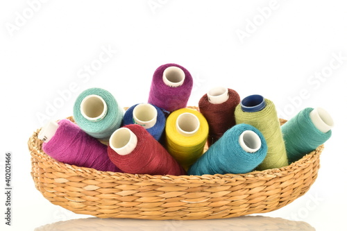Several spools of colored thread in a straw box, close-up, isolated on white.