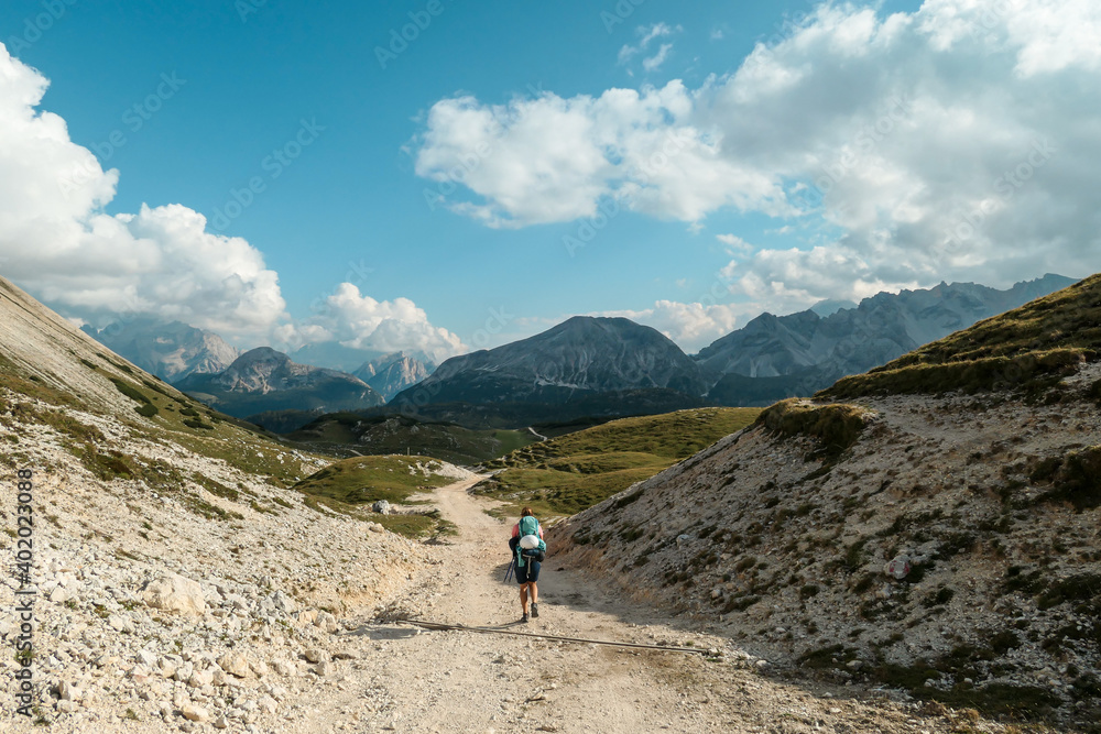 A woman hiking along a high plateau in Italian Dolomites. High mountains around. The area is partially overgrown with grass and partially covered with stones. Remote and desolate area. Freedom