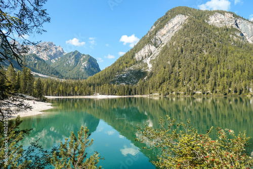 A view on the Pragser Wildsee  a lake in South Tyrolean Dolomites. High mountain chains around the lake. The sky and mountains are reflecting in the lake. Dense forest at the shore. Autumn vibe. Relax