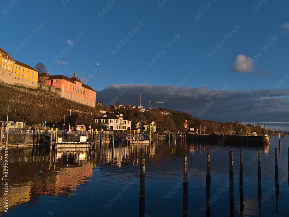 Beautiful view of port basin of town Meersburg, Germany on the shore of Lake Constance in the evening light in winter season with historic buildings and vineyards on the slopes.
