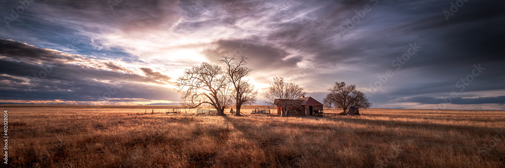An old farmhouse on the eastern plains of Colorado in a rural setting at sunset. The sky is dramatic with wispy clouds. The old house if falling apart and abandoned. An old farmhouse on the eastern plains of Colorado in a rural setting at sunset. The sky is dramatic with wispy clouds. The old house if falling apart and abandoned.