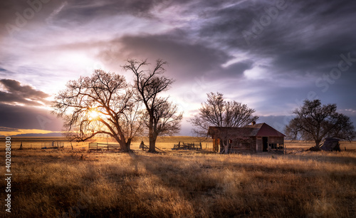 An old farmhouse on the eastern plains of Colorado in a rural setting at sunset. The sky is dramatic with wispy clouds. The old house if falling apart and abandoned. 