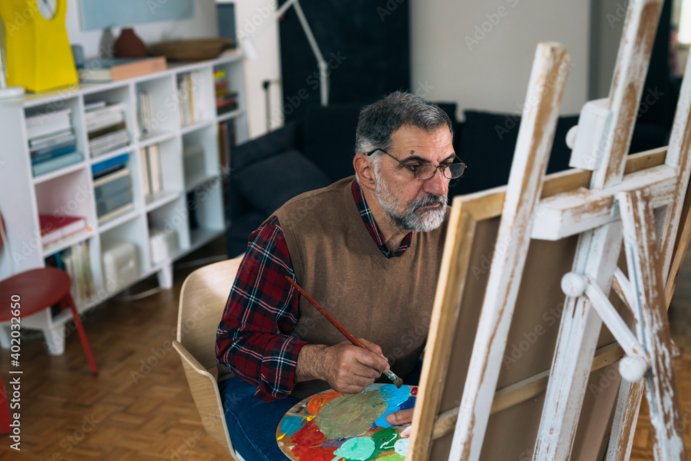 senior man painting a picture in his home senior man painting a picture in his home