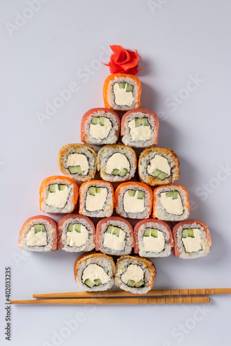 Edible christmas tree made from sushi with salmon, tuna and eel with philadelphia cheese, pickled ginger and sticks for sushi on white. Vertical format. Top view