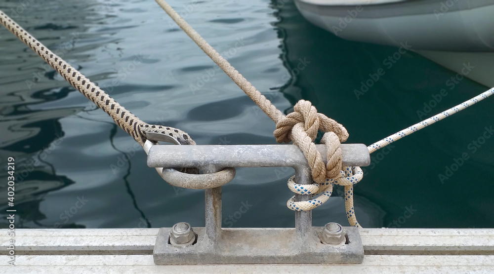 Fototapeta premium Iron mooring with ropes. Nautical ropes close up. Mooring yacht rope with a knotted end tied around a cleat.