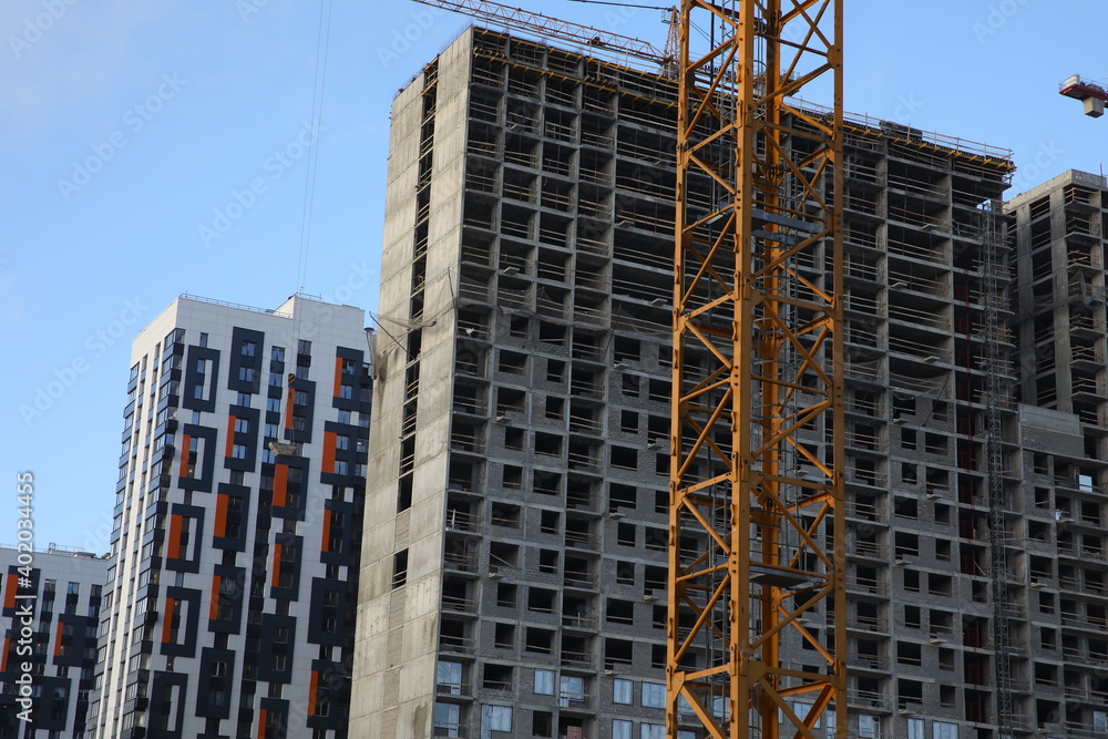 Fototapeta premium Construction of a new house.Unfinished building concrete gray structure many floors windows without glass and a crane on the background of a new white housing with a beautiful finish on the facade