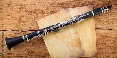 black wooden clarinet  silver woodwind musical brass instrument with old empty vintage music sheet copy space paper on retro oak wood background. classic orchestra symphony background. photo