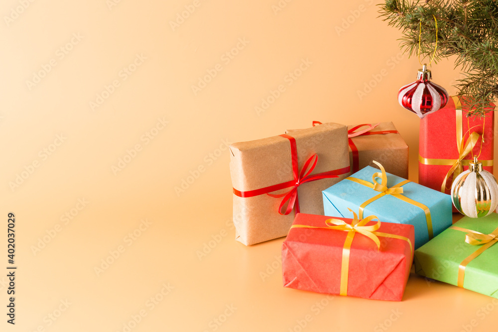 Gifts in beautiful red boxes with gold ribbons under a Christmas tree decorated with glass toys on a beige background. Holiday. New year and Christmas. Banner. Copy space Gifts in beautiful red boxes with gold ribbons under a Christmas tree decorated with glass toys on a beige background. Holiday. New year and Christmas. Banner. Copy space