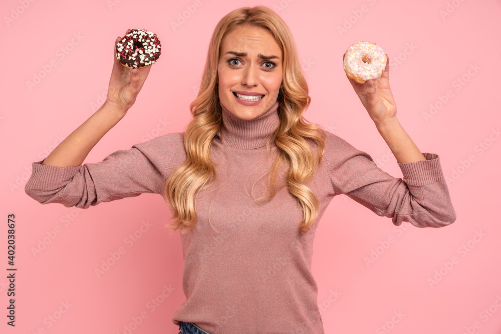 Portrait of a confused young woman showing donuts isolated over pink background Portrait of a confused young woman showing donuts isolated over pink background
