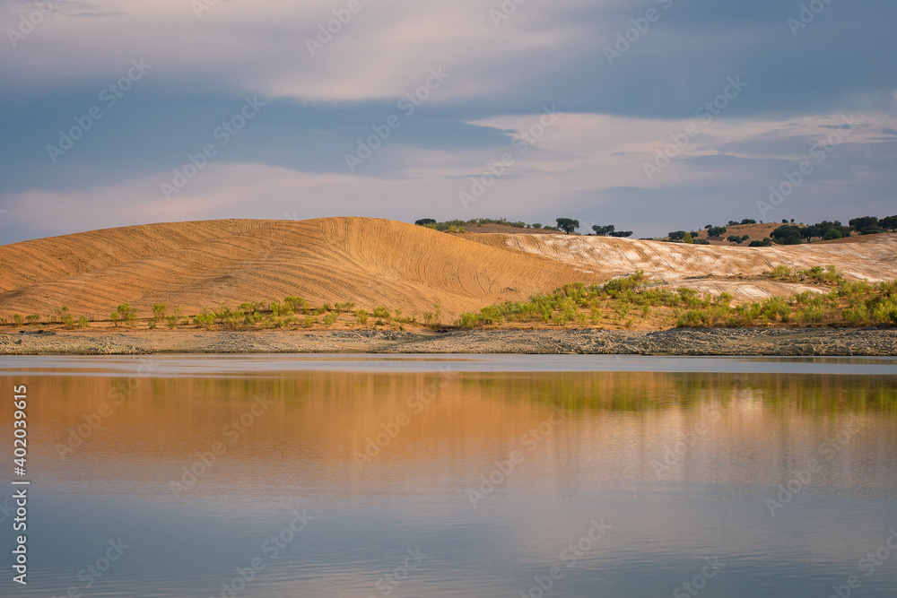 Desert like hill landscape with reflection on the water on a dam lake reservoir at sunset in Terena, Portugal