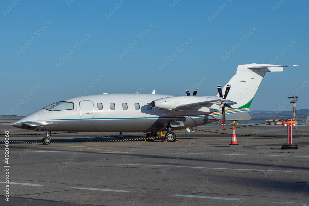 Side view of white business airplane with twin turboprop engines mounted in pusher configuration. Blue sky over the airport. Modern technology in fast transportation, business travel and tourism. Side view of white business airplane with twin turboprop engines mounted in pusher configuration. Blue sky over the airport. Modern technology in fast transportation, business travel and tourism.