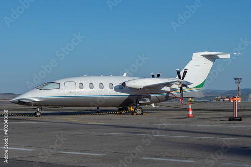 Side view of white business airplane with twin turboprop engines mounted in pusher configuration. Blue sky over the airport. Modern technology in fast transportation, business travel and tourism. 