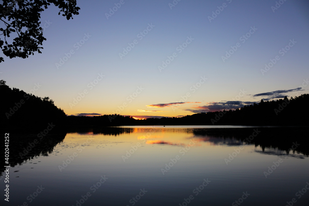 Peaceful evening at the lake. Reflection of the sky and clouds in calm water. Beautiful landscape with Finnish nature.