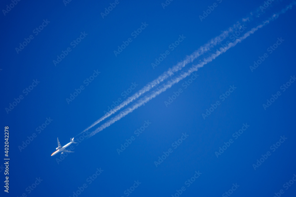 looking up at a Dutch KLM twin engine jet airliner in deep blue sky with vapour trails diagonally across the frame looking up at a Dutch KLM twin engine jet airliner in deep blue sky with vapour trails diagonally across the frame